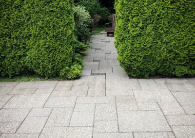 Concrete paving slab driveway in ashlar pattern with garden path and hedging