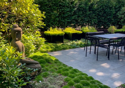 Buddha statue in moss garden with stone terrace and dining table