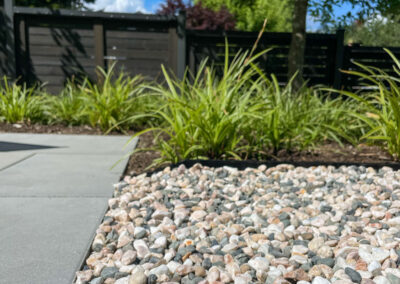 Decorative gravel and ornamental grass planting detail — concrete paving edge with textural planting bed, residential landscape design in East Vancouver by 161 Design Studio.